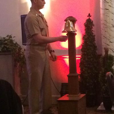 A uniformed navy officer ringing a ceremonial bell.