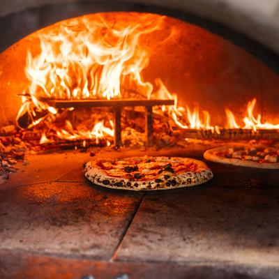 Two pizzas cooking inside a wood-fired oven.