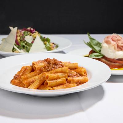 Rigatoni Bolognese served alongside other dishes in the background.