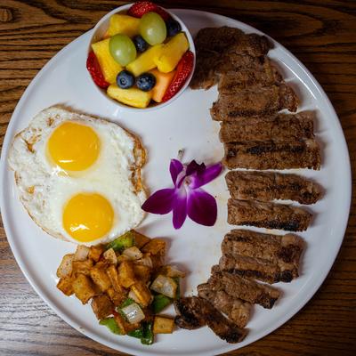 Steak, fried eggs, breakfast potatoes, and a bowl of fruit.