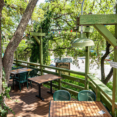 Wooden patio deck with wooden tables,  green chairs, and trees.