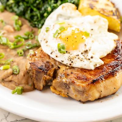 Grilled pork chop, with a fried egg, sauteed collard greens, and puree beans.