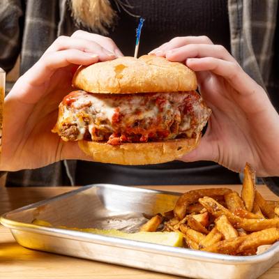 A person enjoys a burger and fries with a glass of beer.