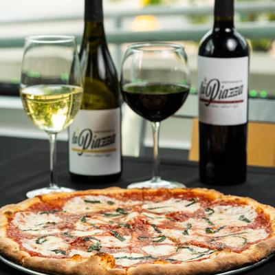 Large pizza Margherita set on a dark tablecloth with red and white wine.