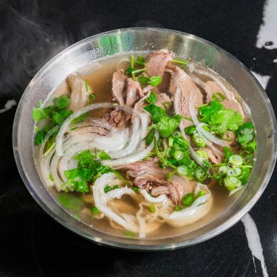 Steaming soup with beef slices, onions, and fresh herbs.