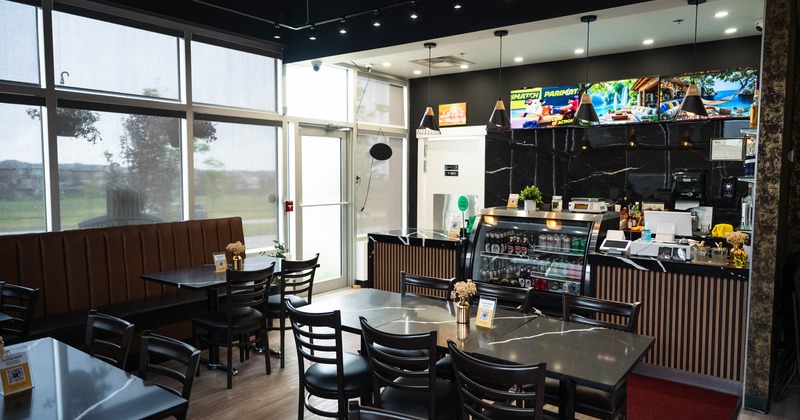Modern café interior with black tables, cushioned seating, and a counter with a refrigerated case