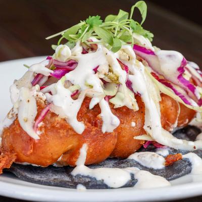 Fried fish taco topped with cabbage slaw, white sauce and microgreens.