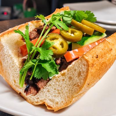 A banh mi sandwich with meat, cucumber, carrot, jalapeno and cilantro on a white plate..