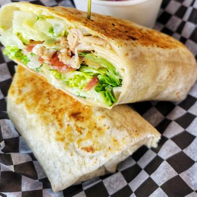 Toasted chicken wrap served on a checkered wax paper with a dip.