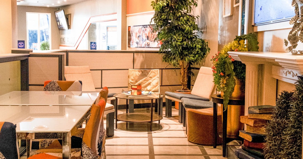 Cafe interior with tables, chairs, plants, and a TV