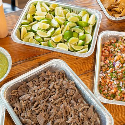 Aluminum trays filled with lime, seasoned beef, pico de gallo, and tortilla chips.