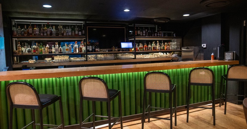 A bar with green-panelled front, high stools