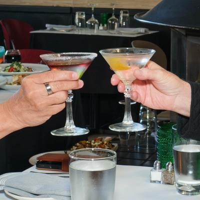Two people toasting with martini glasses at the table.