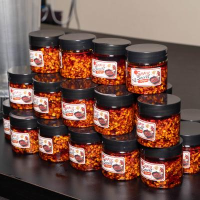 Stacked jars of red chili flakes on a black shelf.