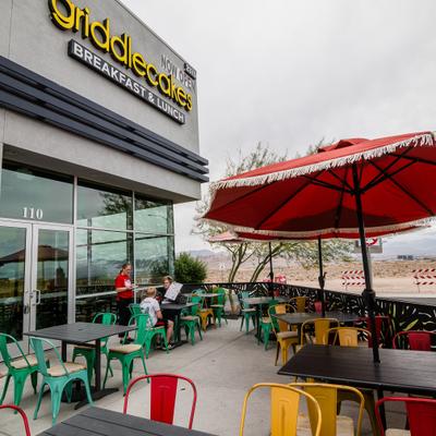 Outdoor restaurant patio with colorful chairs and red umbrellas.