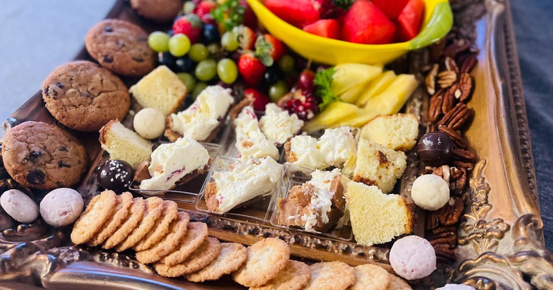 A platter with cookies, fruits, nuts and cake bites