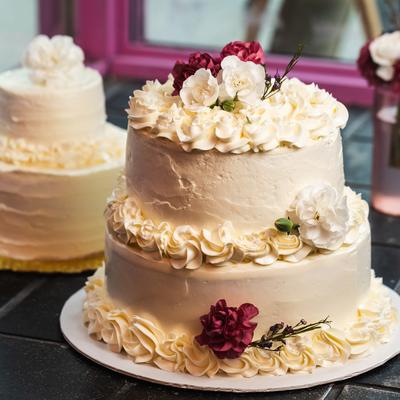 A two-tiered white cake with delicate cream swirls and red and white flowers on top.