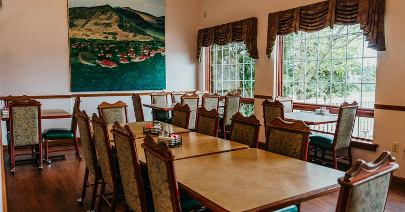 Interior seating area with wooden tables, upholstered chairs and a large landscape painting