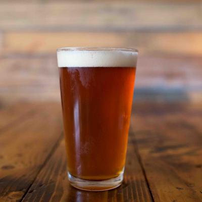 Amber beer in a clear pint glass with foamy head on a wooden wooden table.