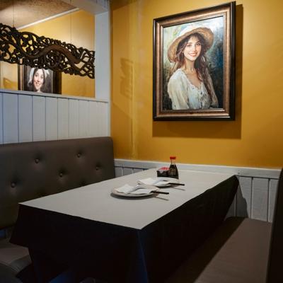 Restaurant booth with white tablecloth, framed art painting on yellow wall..