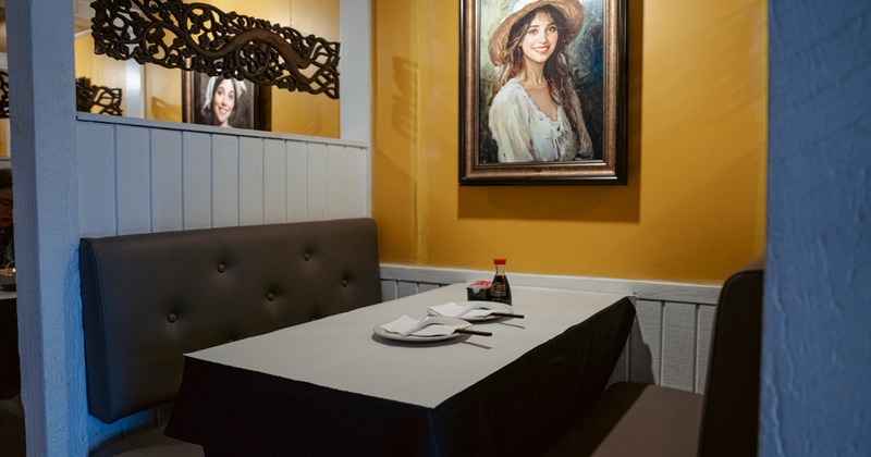Restaurant booth with white tablecloth, framed art painting on yellow wall.