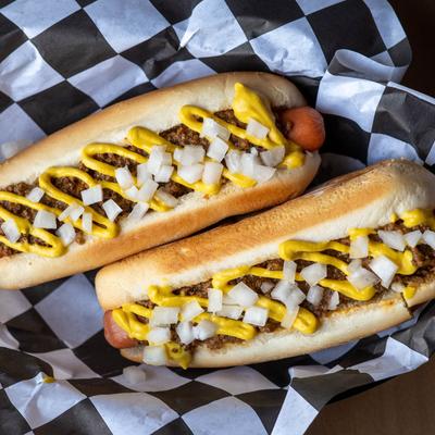 Two hot dogs with meat sauce, onion, and mustard.