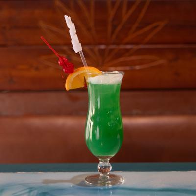 Green cocktail served in a hurricane glass, garnished with orange slice and cherries