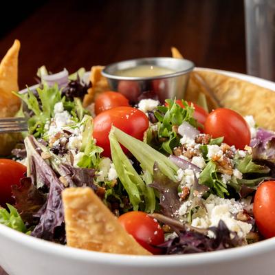 Close up of mixed salad with tomatoes, cheese and dressing on the side.