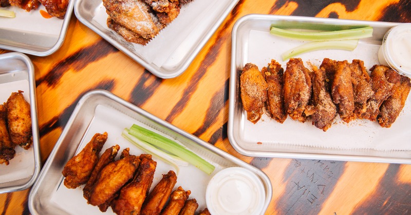 Trays of assorted chicken wings with celery sticks and ranch on a wooden table