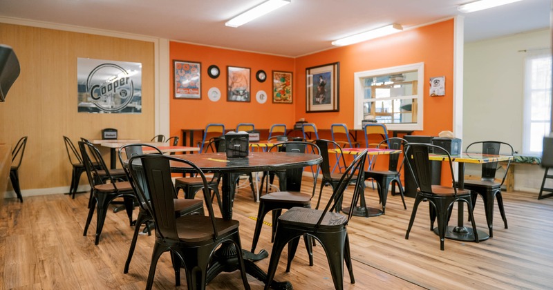 Café-style dining area with black tables and chairs, warm orange and beige walls, and wall decorations