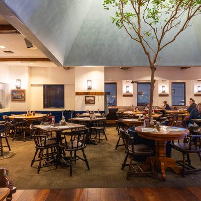 Interior with a tree, wooden tables around it, and walls with art and light.