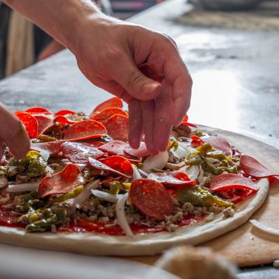 Hands puting toppings on pizza.