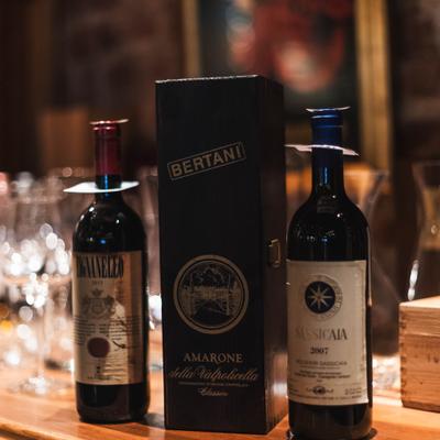 Two wine bottles beside glassware on a wooden table.
