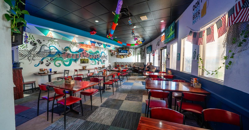 Interior of a vibrant restaurant with colorful murals, red chairs, and wooden tables