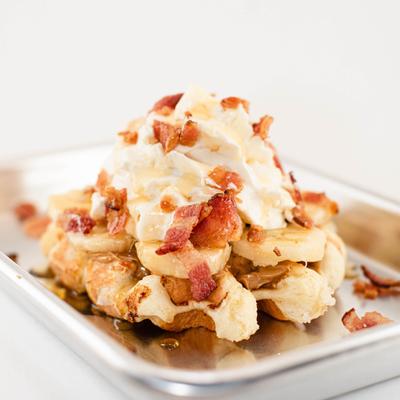 Waffles topped with slices of banana, whipped cream and bacon pieces.