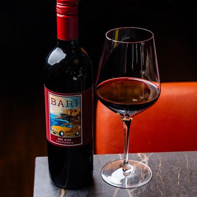 A bottle of red wine with a stemmed glass filled with red wine.