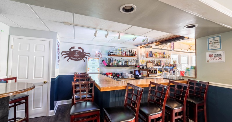Interior of a bar with a wooden counter, bar stools, and shelves with liquor bottles