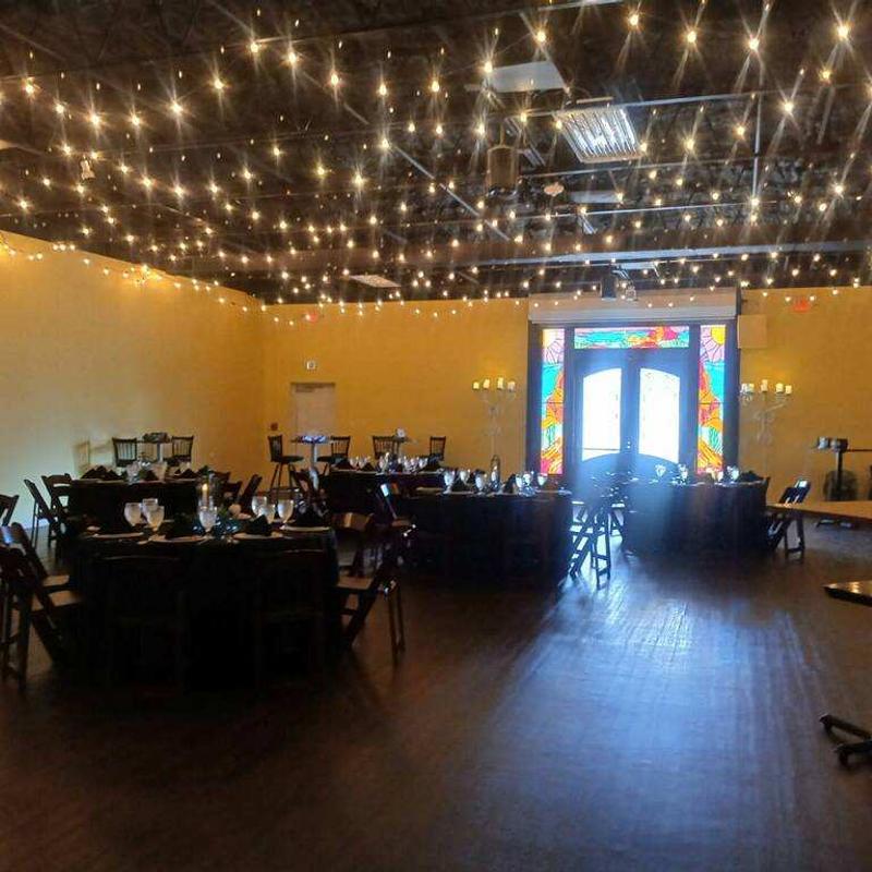 Event room with string lights overhead and round tables set for dining