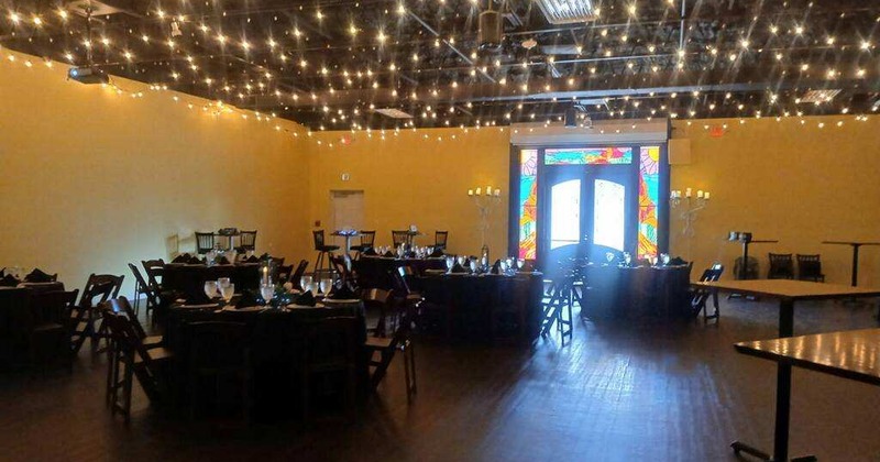 Event room with string lights overhead and round tables set for dining