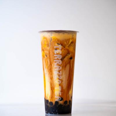 A tall, clear cup of creamy boba milk tea with swirling caramel tones.