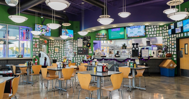 Colorful interior - tables, pendant lights, framed artwork, digital menu boards & a service counter.