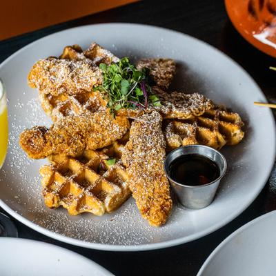 Chicken and Waffles served with syrup and topped with powdere sugar and microgreens.