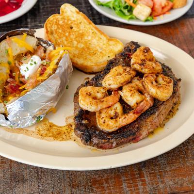Shrimp-topped steak served with baked potato and piece of toast.