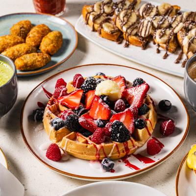 Waffle topped with mixed berries and sweet drizzle, surrounded by brunch dishes.