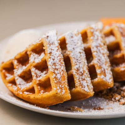 Belgian Waffle on a white plate, topped with powdered sugar.