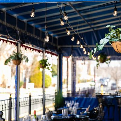 Covered outdoor dining area, decorated with hanging plants and string lights.
