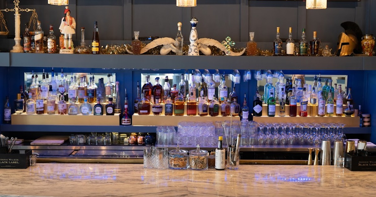 A well-stocked bar with shelves displaying various liquor bottles, glasses hanging above
