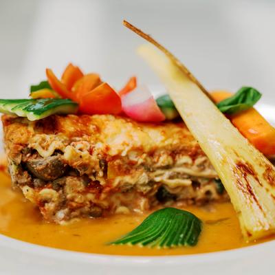 Lasagna with vegetable garnish and sauce on a white plate, close up.