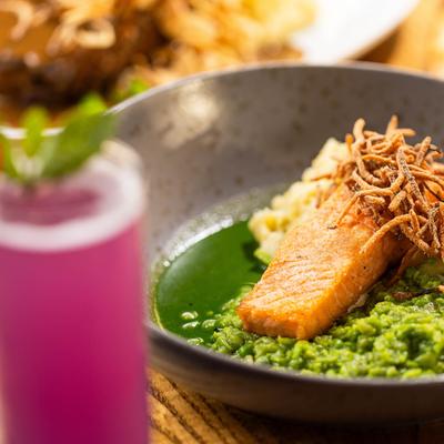 Seared salmon on green puree, topped with crispy shallots, served with a purple cocktail.