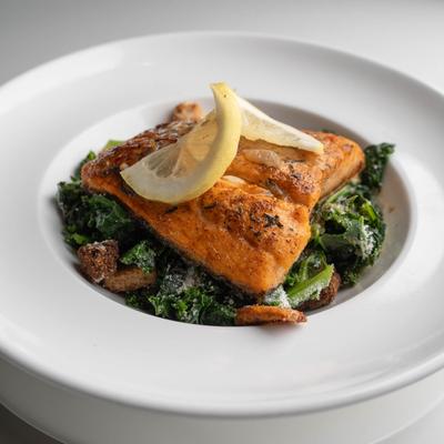 Grilled salmon with lemon slices over sauteed greens.